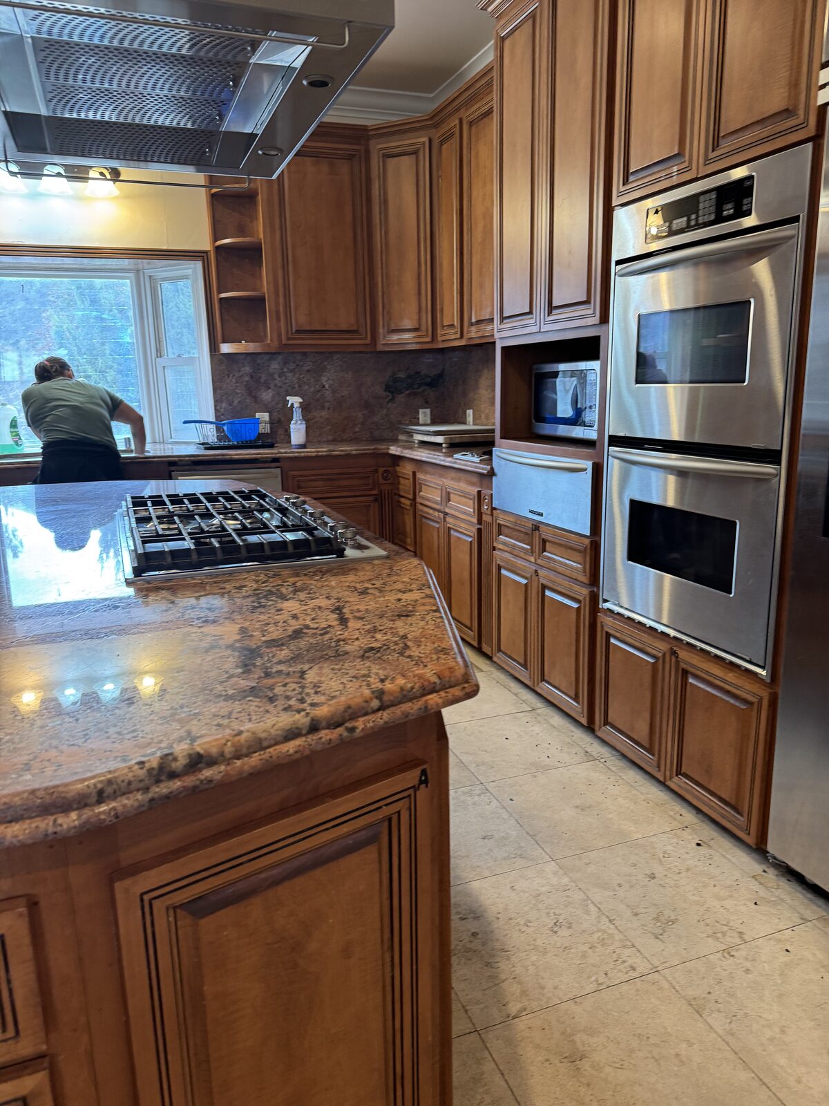 Scrub Bros team member cleaning a kitchen with wood cabinetry and granite counters