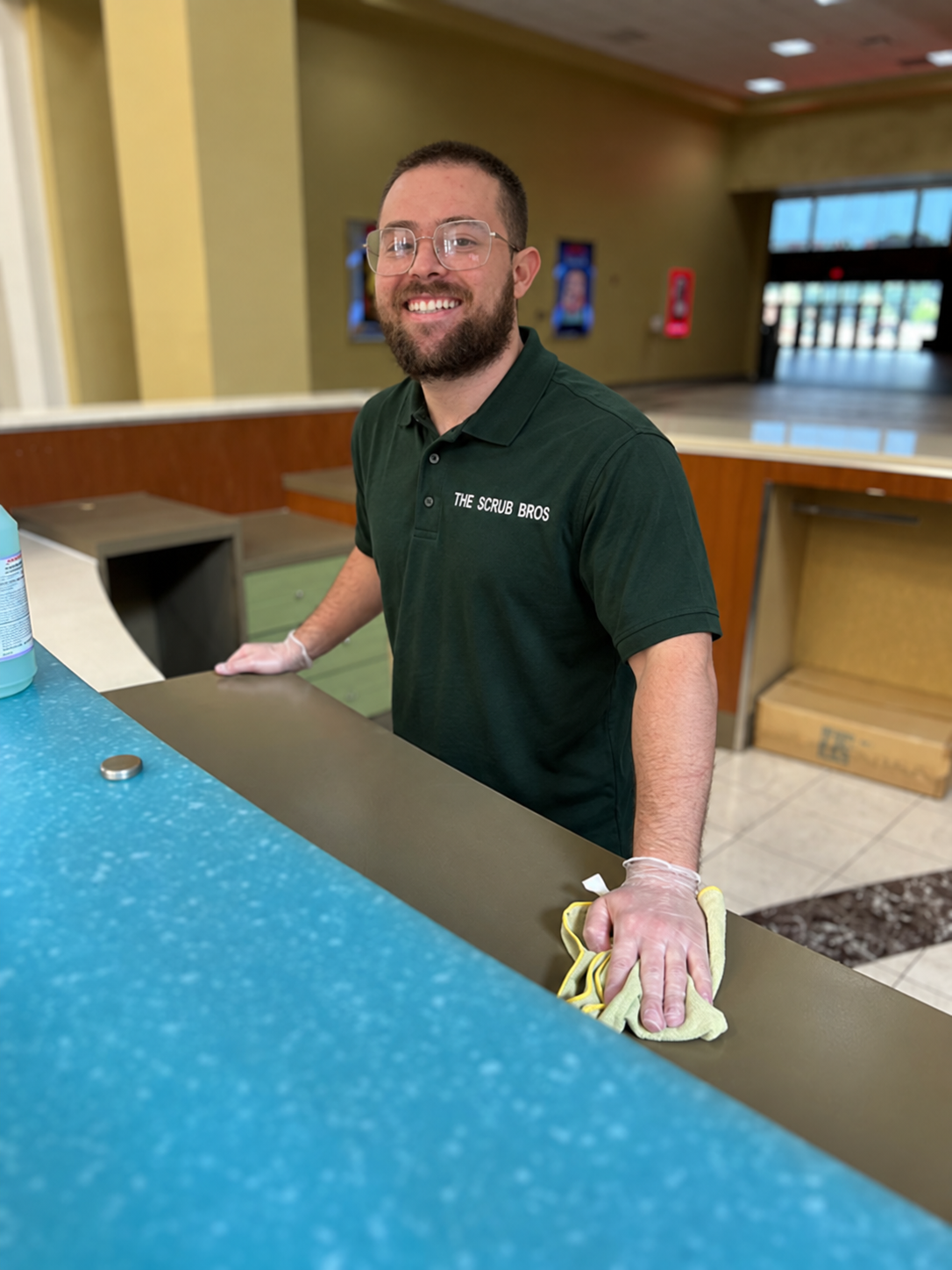 Scrub Bros team member wiping down a reception counter in a Scrub Bros polo shirt